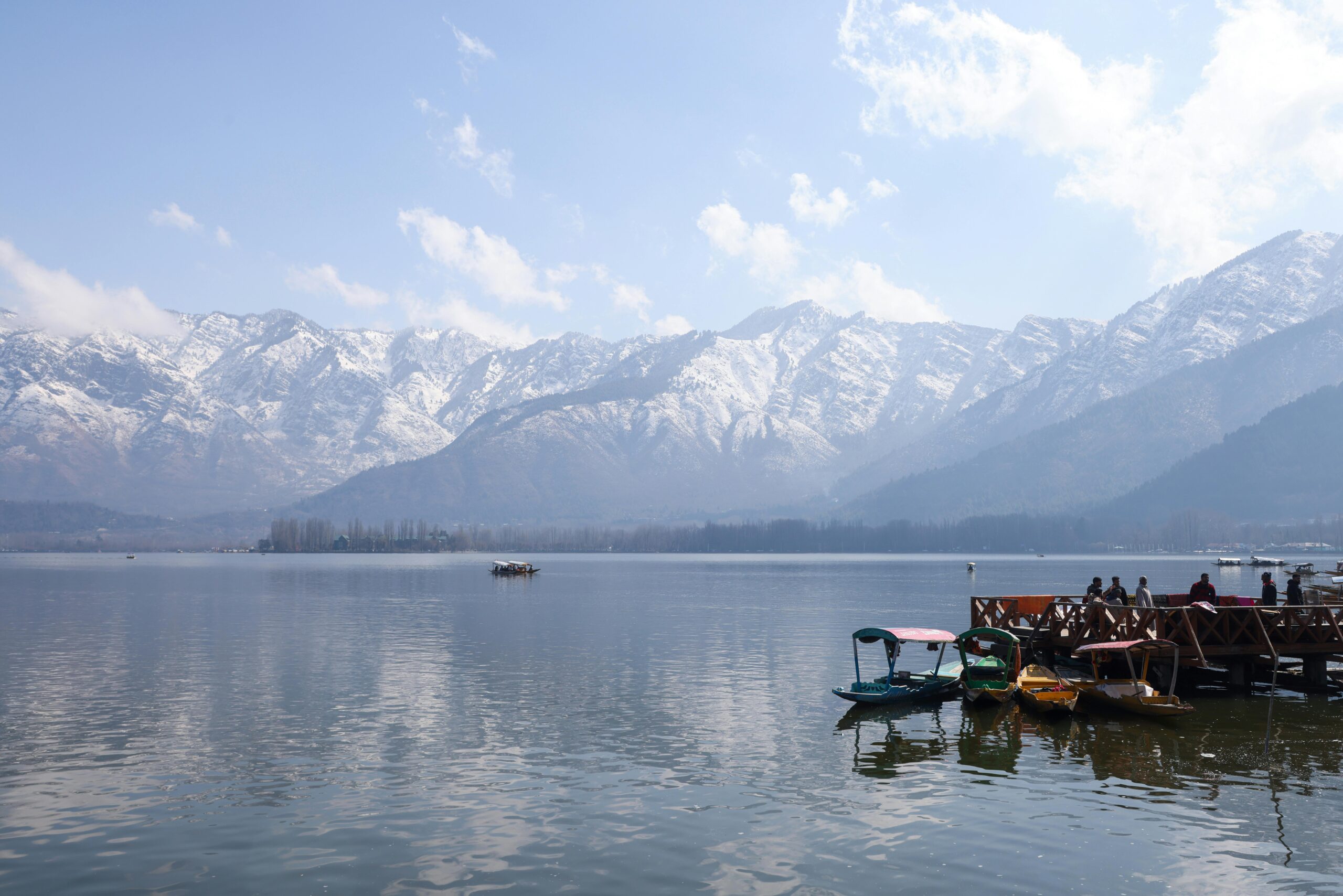 Boats on Dal Lake with snowcapped Himalayas in the background, serene Srinagar scene.