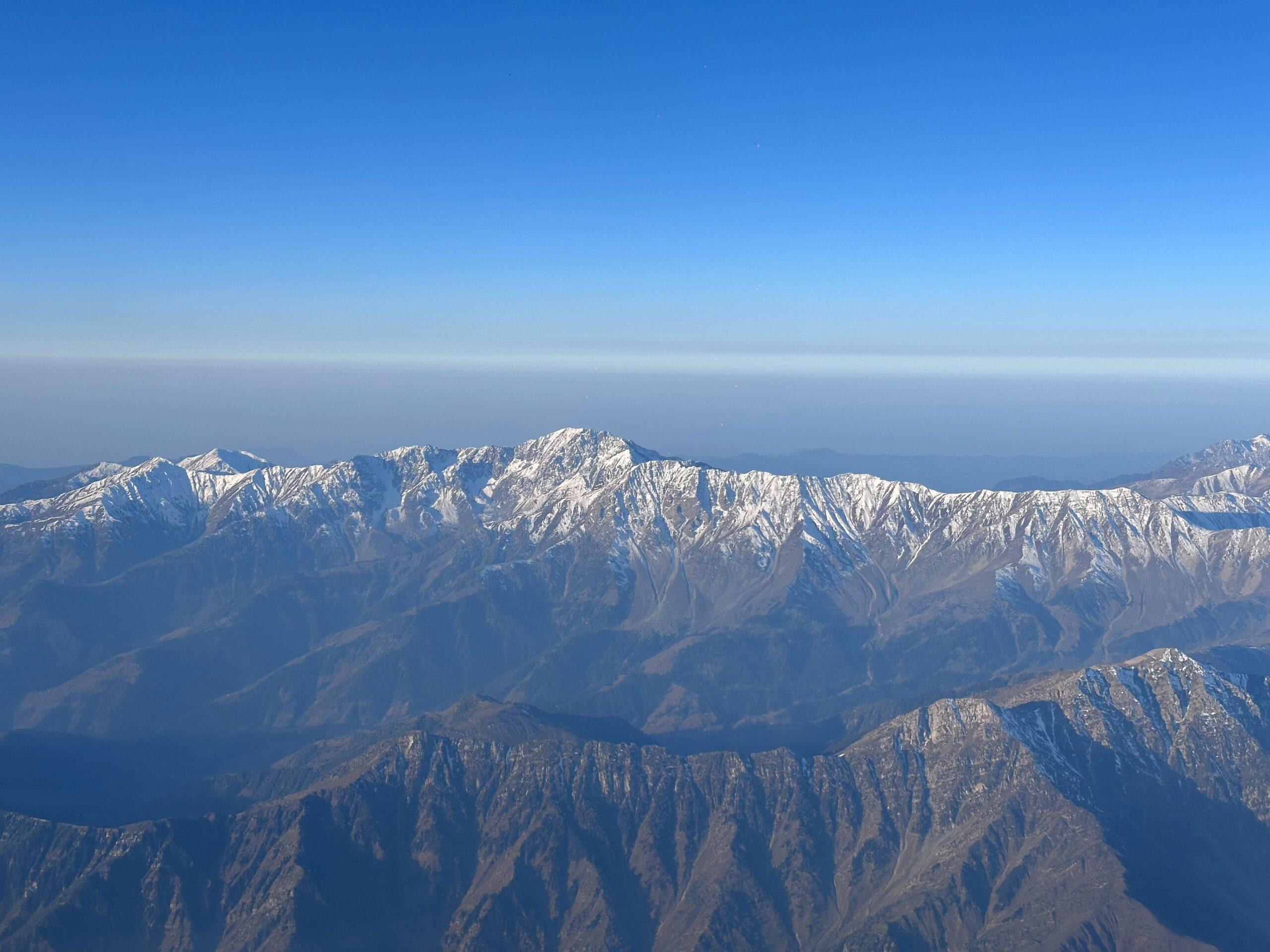 Breathtaking aerial view of the snow-capped Pir Panjal mountain range under a clear blue sky.
